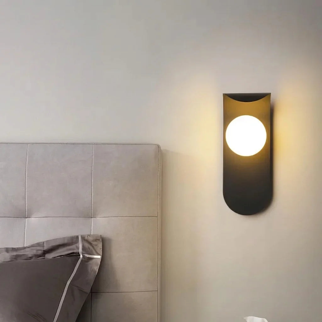 Fekete gömbös LED lámpa egy szürke kárpitozott ágytámla mellett