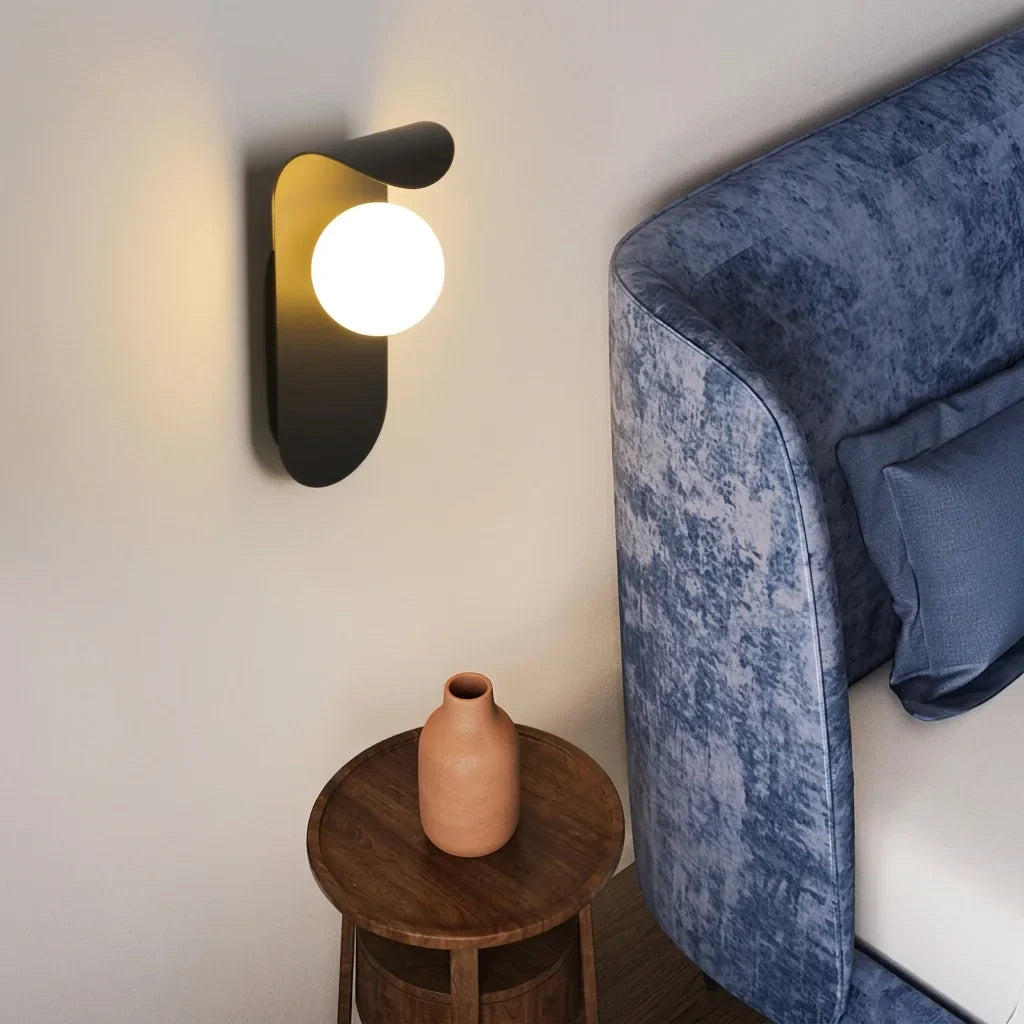 Fekete gömbös LED lámpa egy fa kisasztal fölött, kék bársony ágy mellett
