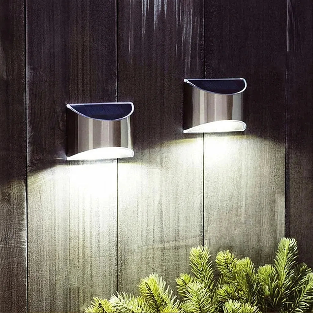 Két inox napelemes lámpa egy sötét fa kerítést világít meg