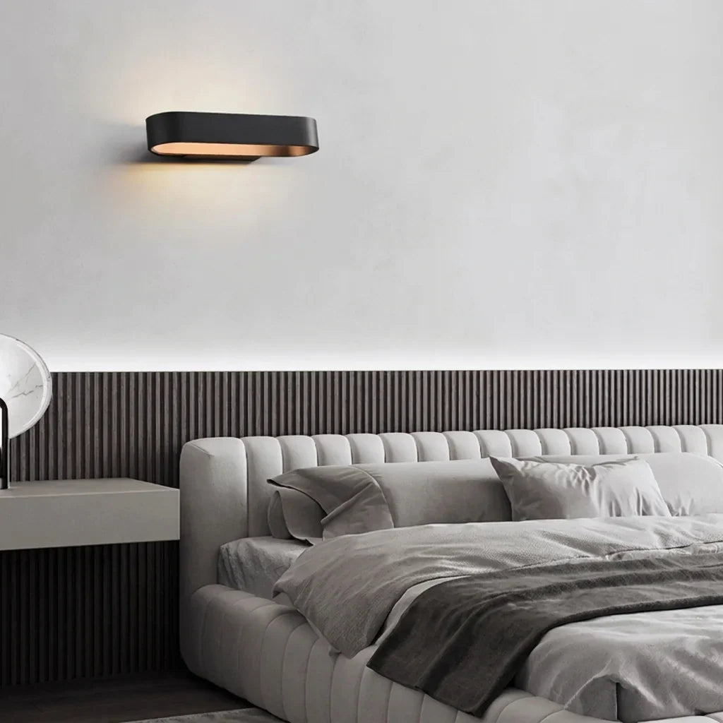 Fekete ovális LED lámpa egy szürke kárpitozott ágy fölött