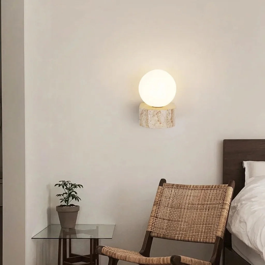 Travertin talpas gömb lámpa egy ágy és egy rattan fotel mellett
